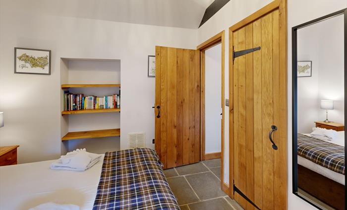 A cosy double bedroom with a check throw, wooden doors, a built-in bookshelf, and bedside lamps